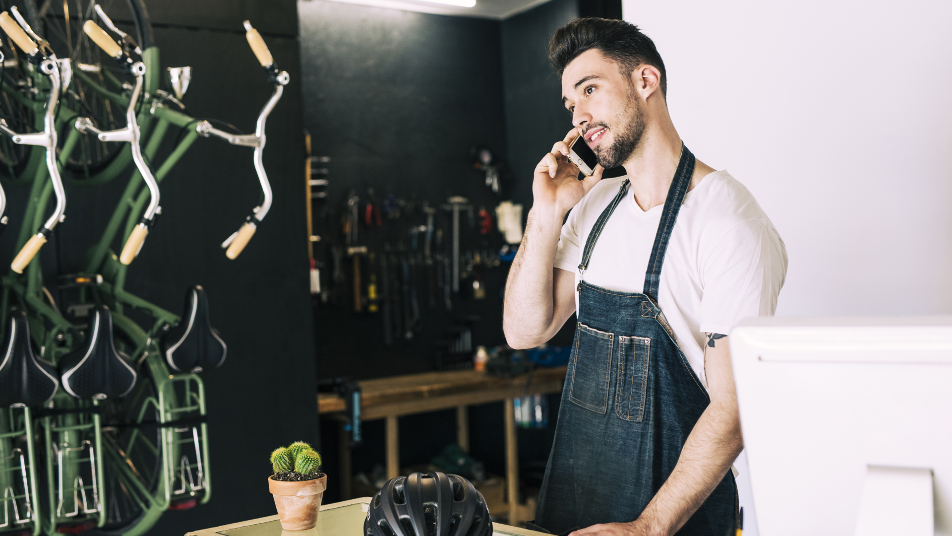 Pareja sonriente de dueños o trabajadores de un negocio con delantales negros, posando en la entrada de una tienda con puerta de vidrio. En la puerta cuelga un cartel que dice 'ABIERTO